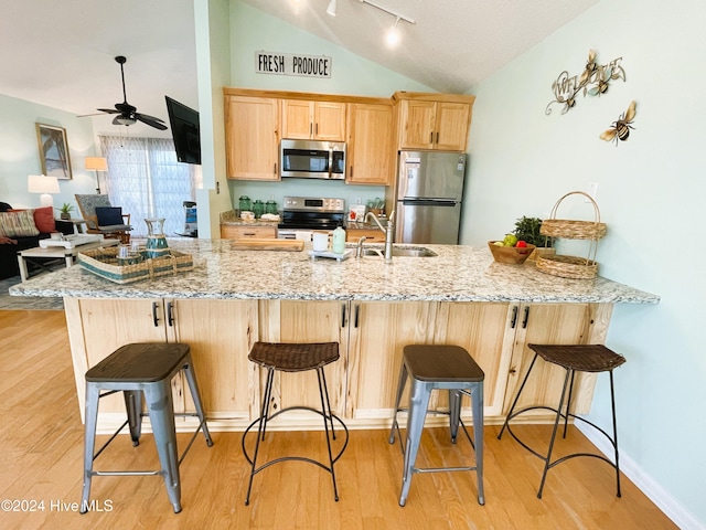 kitchen featuring a kitchen breakfast bar, stainless steel appliances, sink, light wood-type flooring, and light brown cabinetry