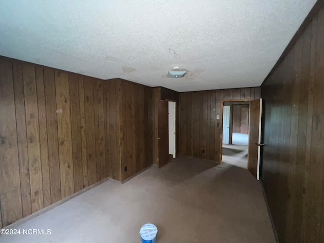 interior space featuring wooden walls, a textured ceiling, and light colored carpet