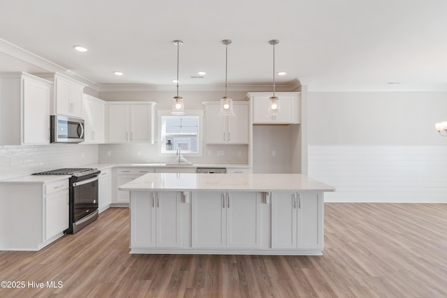 kitchen with pendant lighting, appliances with stainless steel finishes, white cabinetry, a kitchen island, and light wood-type flooring