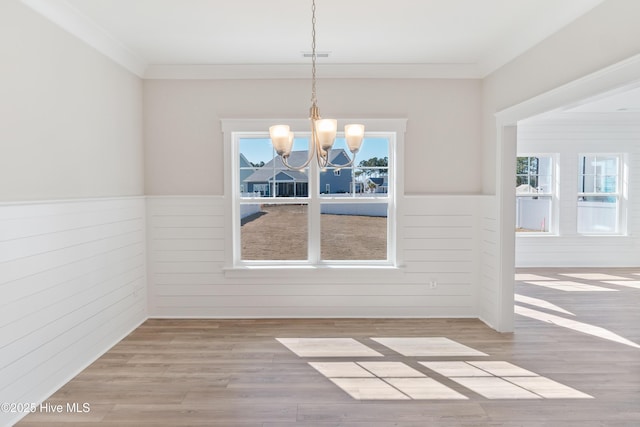 unfurnished dining area with light wood-style floors, a healthy amount of sunlight, and wainscoting