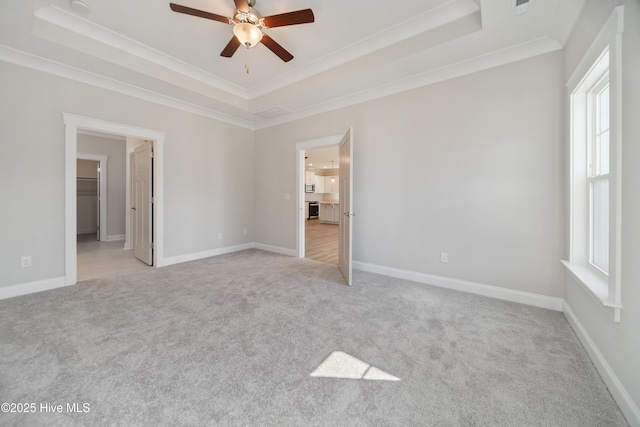 unfurnished bedroom featuring light carpet, baseboards, a spacious closet, a tray ceiling, and crown molding