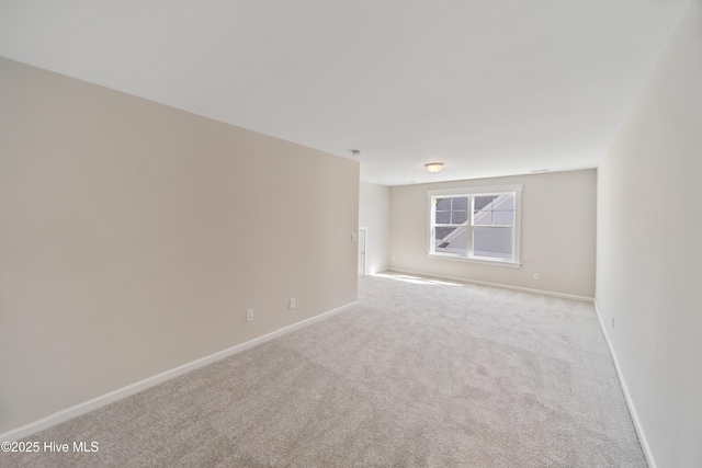 spare room featuring light colored carpet and baseboards