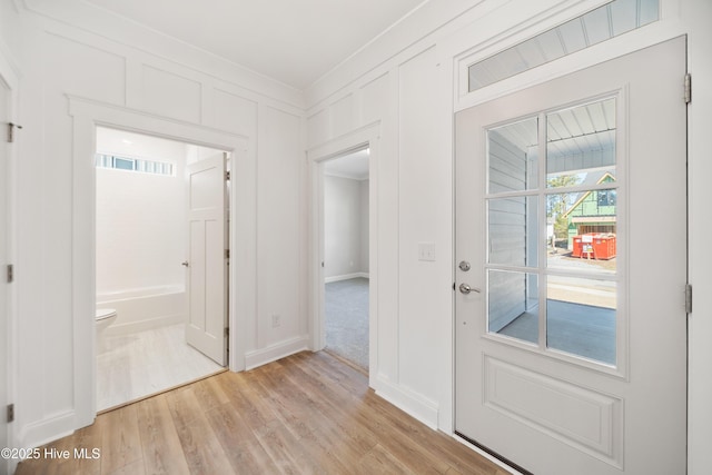 entryway featuring light wood-type flooring, visible vents, a decorative wall, and crown molding