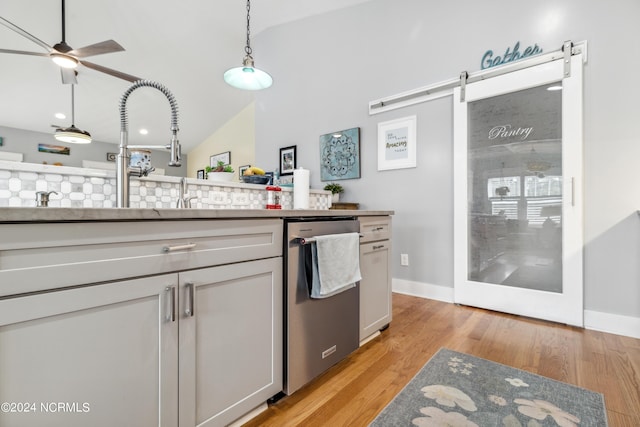 kitchen with lofted ceiling, hanging light fixtures, stainless steel dishwasher, a barn door, and light wood-type flooring