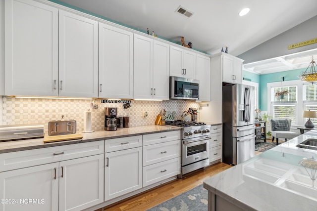 kitchen featuring light hardwood / wood-style flooring, vaulted ceiling, decorative backsplash, white cabinets, and appliances with stainless steel finishes