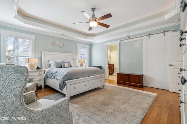 bedroom featuring ceiling fan, light wood-type flooring, ensuite bathroom, and a tray ceiling