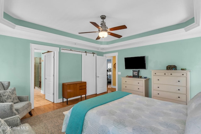 910 Old Dow Rd, Carolina Beach, NC 28428 - bedroom featuring a raised ceiling, wood finished floors, crown molding, a barn door, and a ceiling fan
