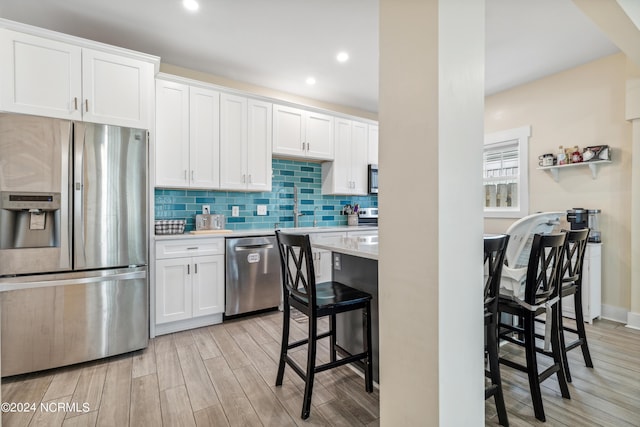 kitchen with a breakfast bar, light wood-type flooring, appliances with stainless steel finishes, tasteful backsplash, and white cabinetry