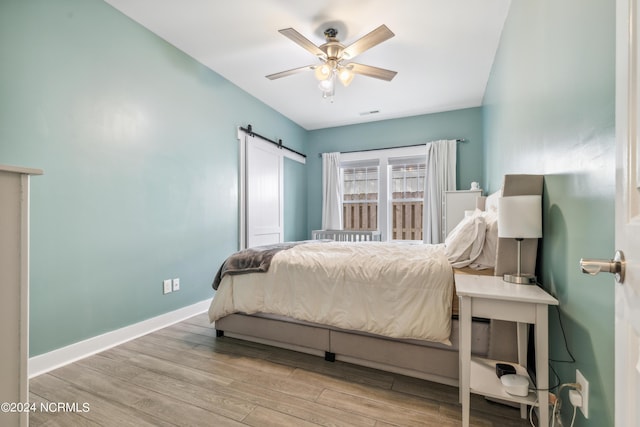 bedroom with ceiling fan, a barn door, and light hardwood / wood-style floors