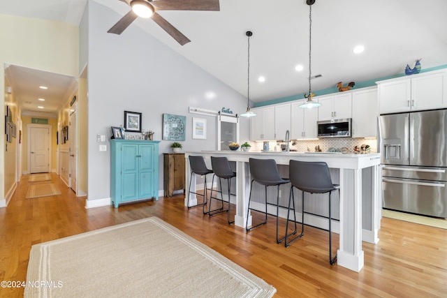 kitchen featuring white cabinetry, backsplash, decorative light fixtures, a center island with sink, and appliances with stainless steel finishes