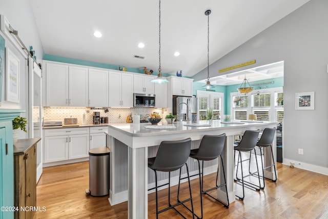 kitchen featuring pendant lighting, a center island with sink, a barn door, appliances with stainless steel finishes, and white cabinetry