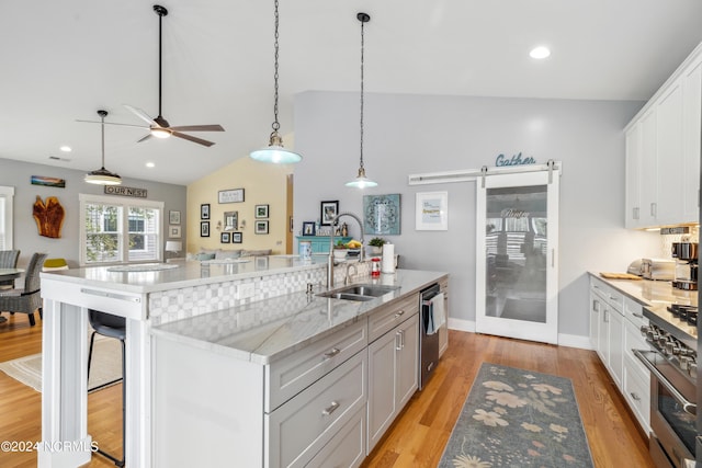 kitchen featuring sink, stainless steel appliances, a barn door, a center island with sink, and white cabinets