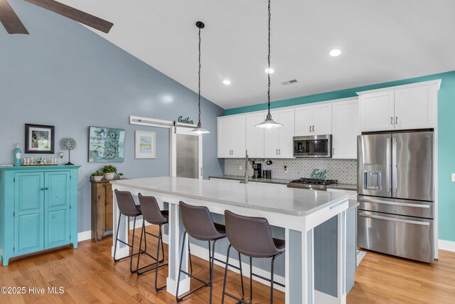 910 Old Dow Rd, Carolina Beach, NC 28428 - kitchen with appliances with stainless steel finishes, tasteful backsplash, an island with sink, white cabinets, and light wood-style flooring