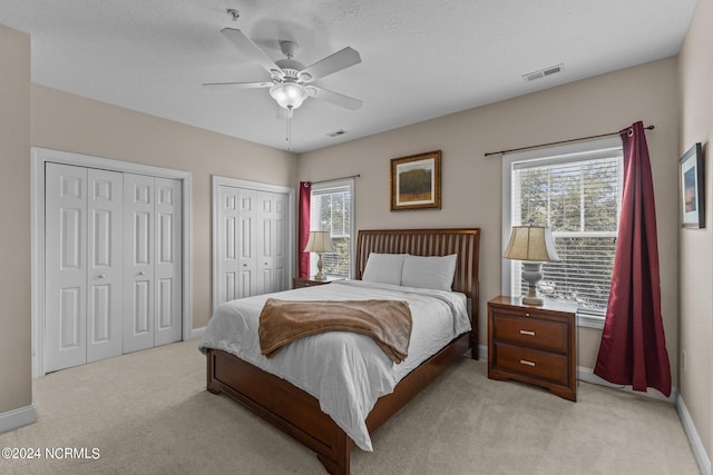 carpeted bedroom featuring multiple windows, a textured ceiling, two closets, and ceiling fan