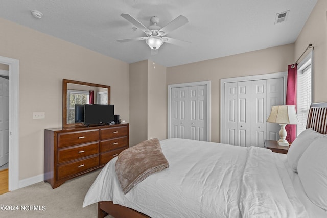 bedroom with ceiling fan, light colored carpet, a textured ceiling, and multiple closets