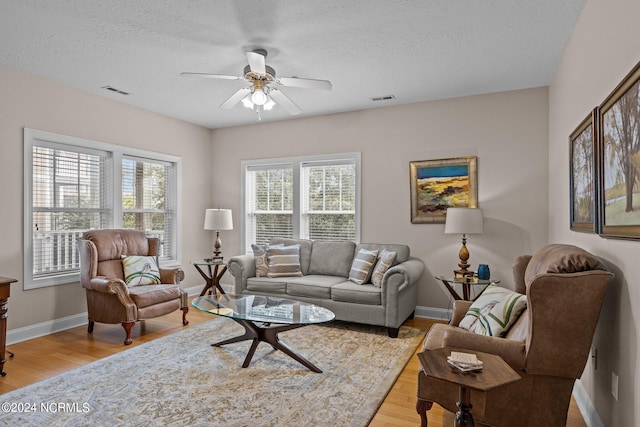 living room featuring light wood-type flooring, ceiling fan, and a textured ceiling