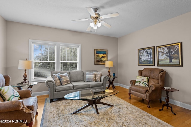 living room featuring light wood-type flooring, ceiling fan, and a textured ceiling