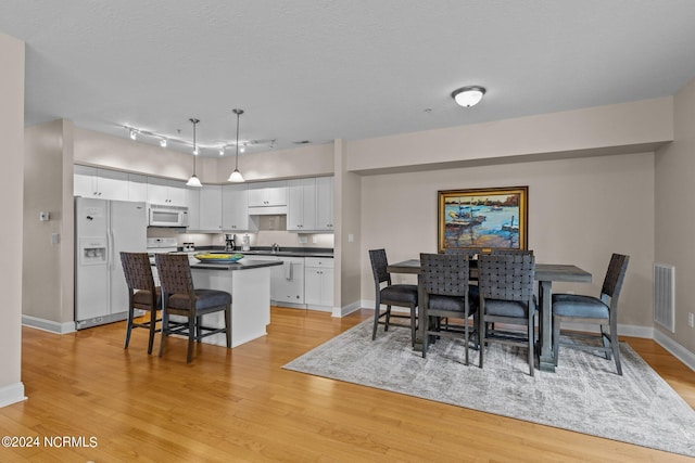 dining space with a textured ceiling, rail lighting, light hardwood / wood-style floors, and sink