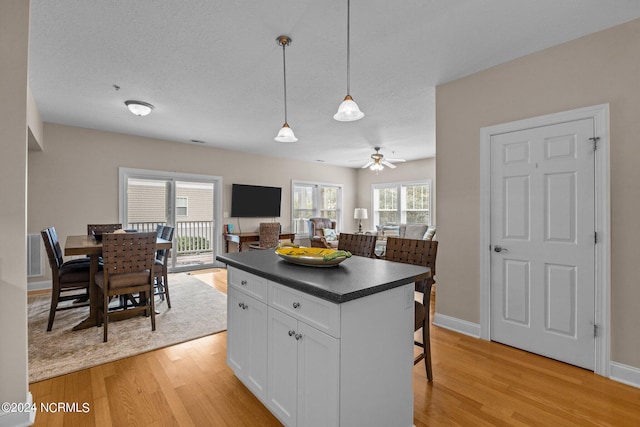 kitchen featuring light hardwood / wood-style floors, a center island, white cabinets, decorative light fixtures, and ceiling fan