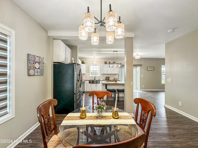 dining space with sink, dark wood-type flooring, and an inviting chandelier