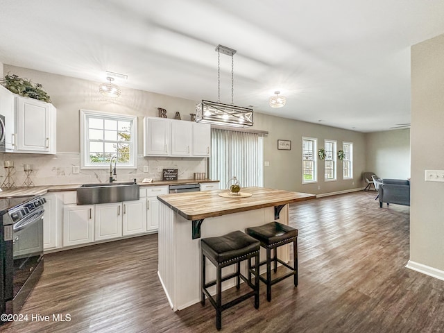 kitchen featuring electric range, white cabinetry, sink, a center island, and butcher block countertops