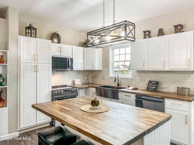 kitchen featuring appliances with stainless steel finishes, white cabinetry, sink, a center island, and butcher block countertops