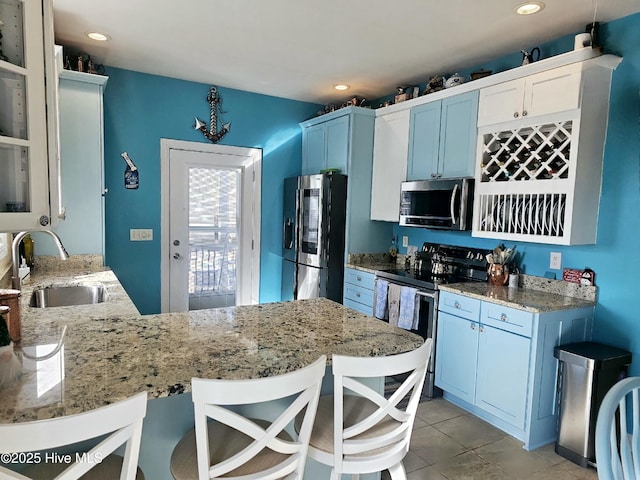 kitchen with kitchen peninsula, sink, blue cabinets, a breakfast bar, and stainless steel appliances