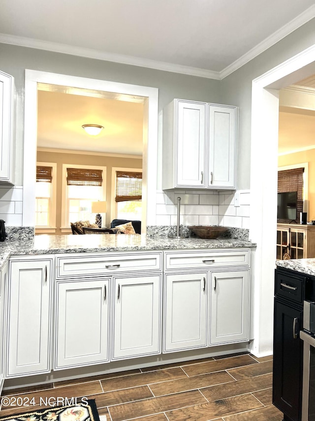 kitchen featuring light stone counters, dark hardwood / wood-style floors, white cabinets, decorative backsplash, and crown molding