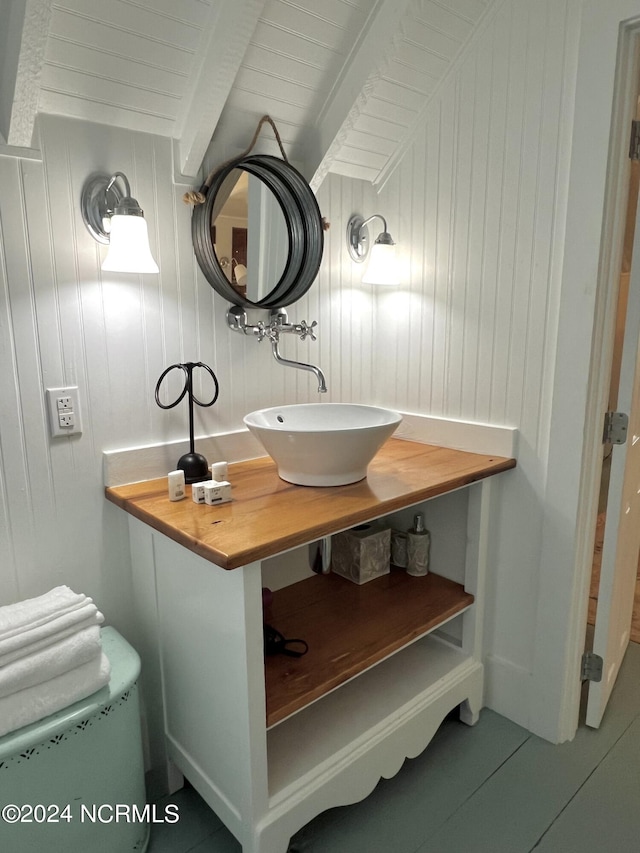 bathroom with vanity, beamed ceiling, wood walls, and tile patterned flooring