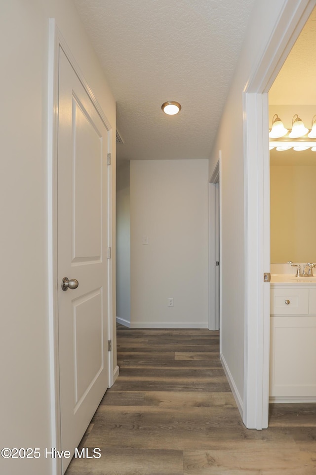 hallway featuring a textured ceiling, baseboards, and wood finished floors