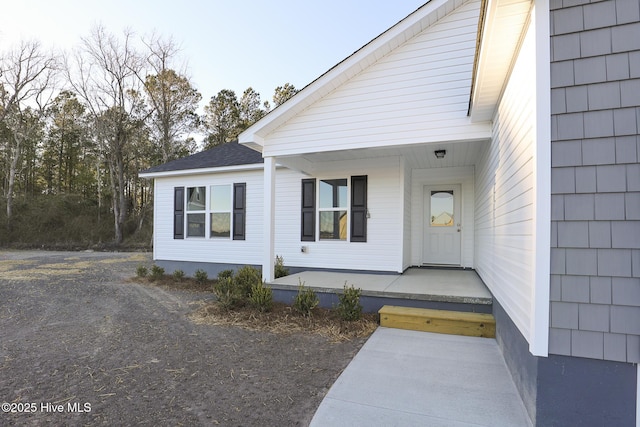 property entrance featuring covered porch and a shingled roof