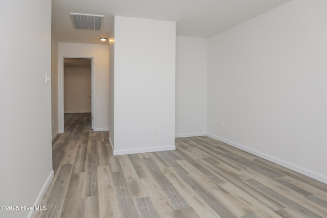 empty room with light wood finished floors, baseboards, visible vents, and a textured ceiling