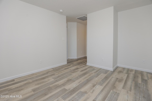 empty room with visible vents, light wood-style flooring, and baseboards