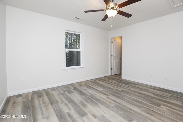 spare room with a textured ceiling, ceiling fan, wood finished floors, visible vents, and baseboards