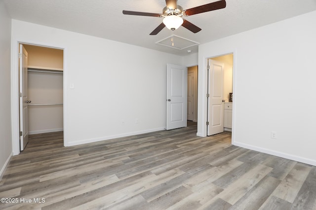 unfurnished bedroom featuring a spacious closet, wood finished floors, and baseboards