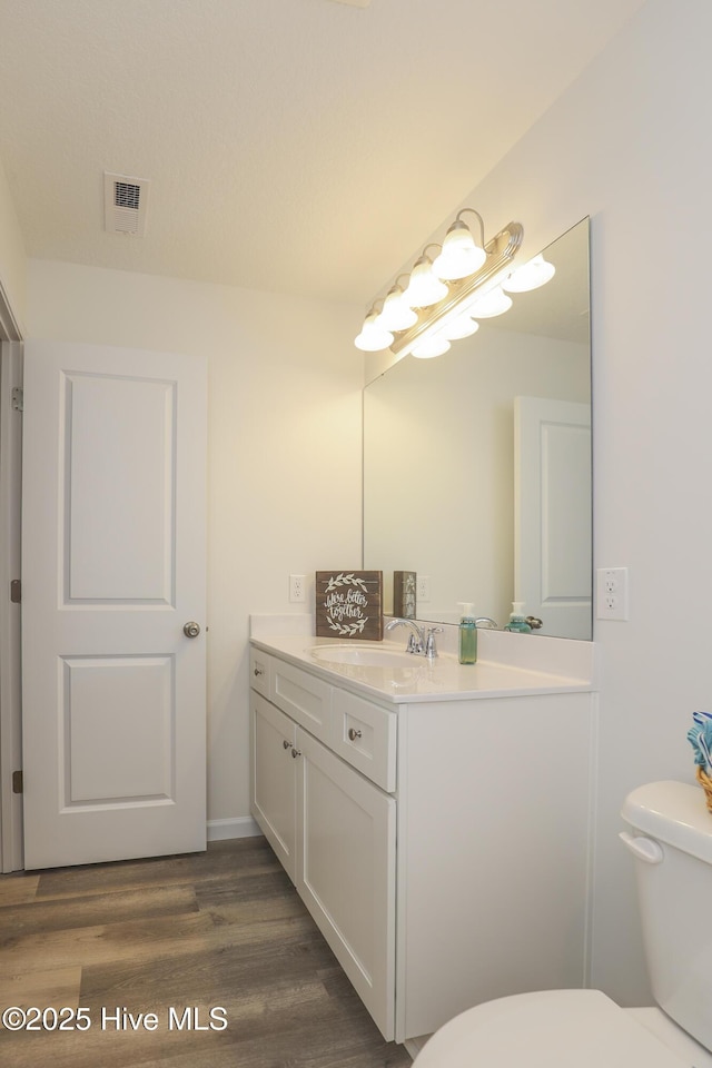 half bathroom featuring visible vents, vanity, toilet, and wood finished floors