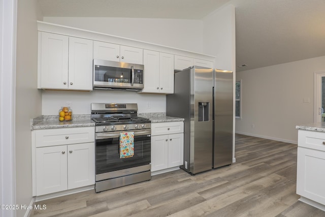 kitchen with stainless steel appliances, white cabinetry, vaulted ceiling, light stone countertops, and light wood-type flooring