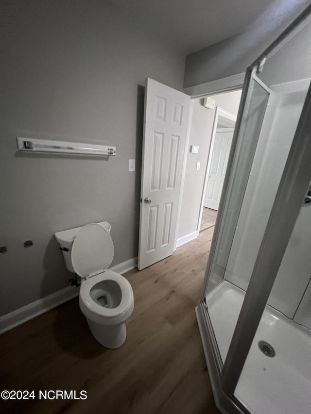 bathroom featuring wood-type flooring, toilet, and a shower with shower door