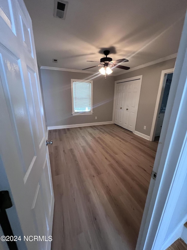 unfurnished bedroom featuring wood-type flooring, ornamental molding, ceiling fan, and a closet