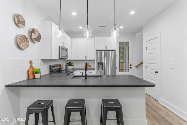 kitchen with a breakfast bar area, kitchen peninsula, sink, white cabinets, and appliances with stainless steel finishes