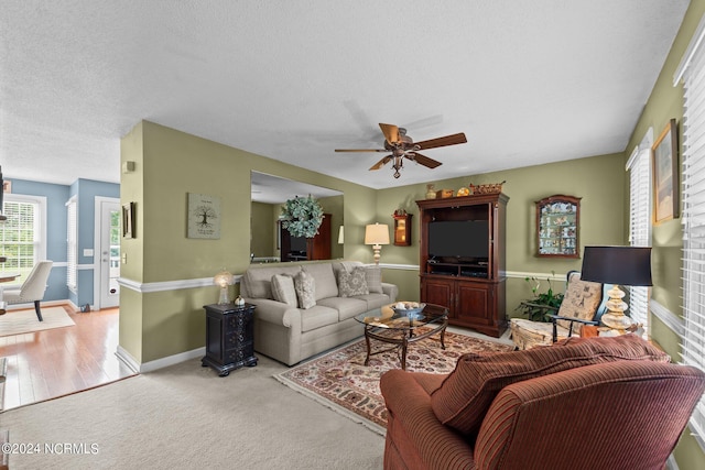 living room with a textured ceiling, ceiling fan, and light hardwood / wood-style flooring