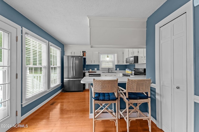 kitchen featuring light wood-type flooring, a healthy amount of sunlight, a breakfast bar area, appliances with stainless steel finishes, and white cabinetry