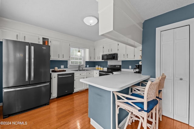 kitchen with kitchen peninsula, a textured ceiling, white cabinetry, black appliances, and light hardwood / wood-style floors