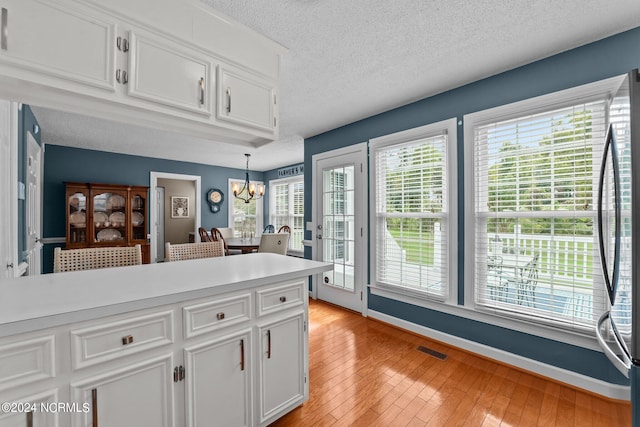 kitchen featuring stainless steel refrigerator, light hardwood / wood-style floors, a notable chandelier, hanging light fixtures, and white cabinetry