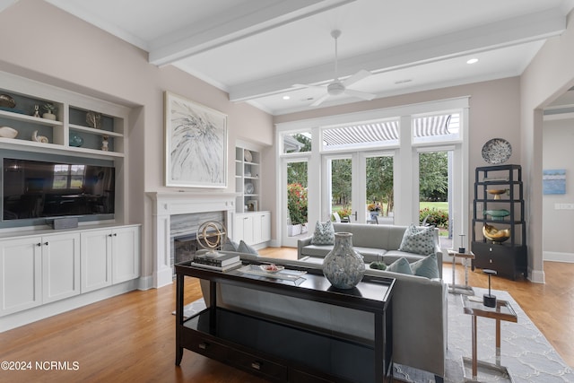 living area featuring built in shelves, a premium fireplace, baseboards, light wood-type flooring, and beamed ceiling