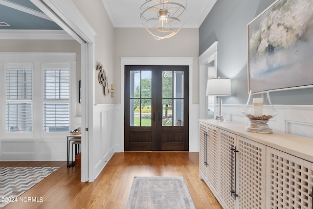 foyer featuring french doors, a wainscoted wall, light wood finished floors, ornamental molding, and a chandelier