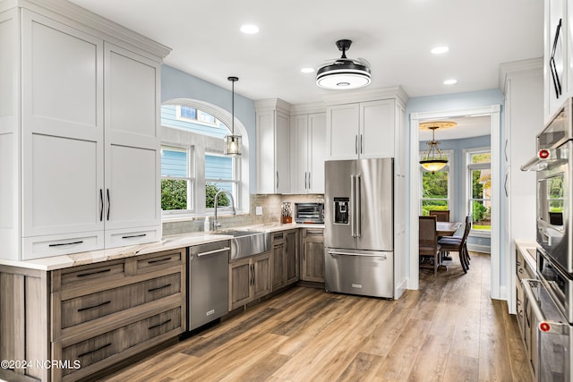 kitchen with light stone counters, white cabinets, decorative light fixtures, appliances with stainless steel finishes, and light hardwood / wood-style floors