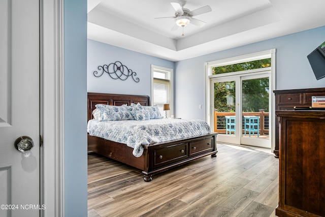 bedroom with wood-type flooring, a tray ceiling, access to exterior, and ceiling fan