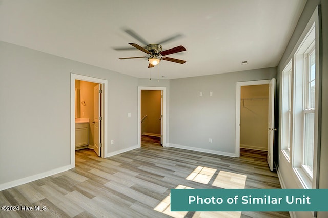 unfurnished bedroom with ceiling fan, ensuite bathroom, a walk in closet, a closet, and light wood-type flooring