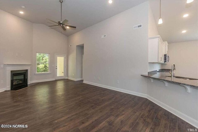 unfurnished living room featuring ceiling fan, dark wood-type flooring, sink, and high vaulted ceiling